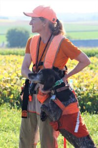 Woman upland hunting guide in orange with a german shorthaired pointer.